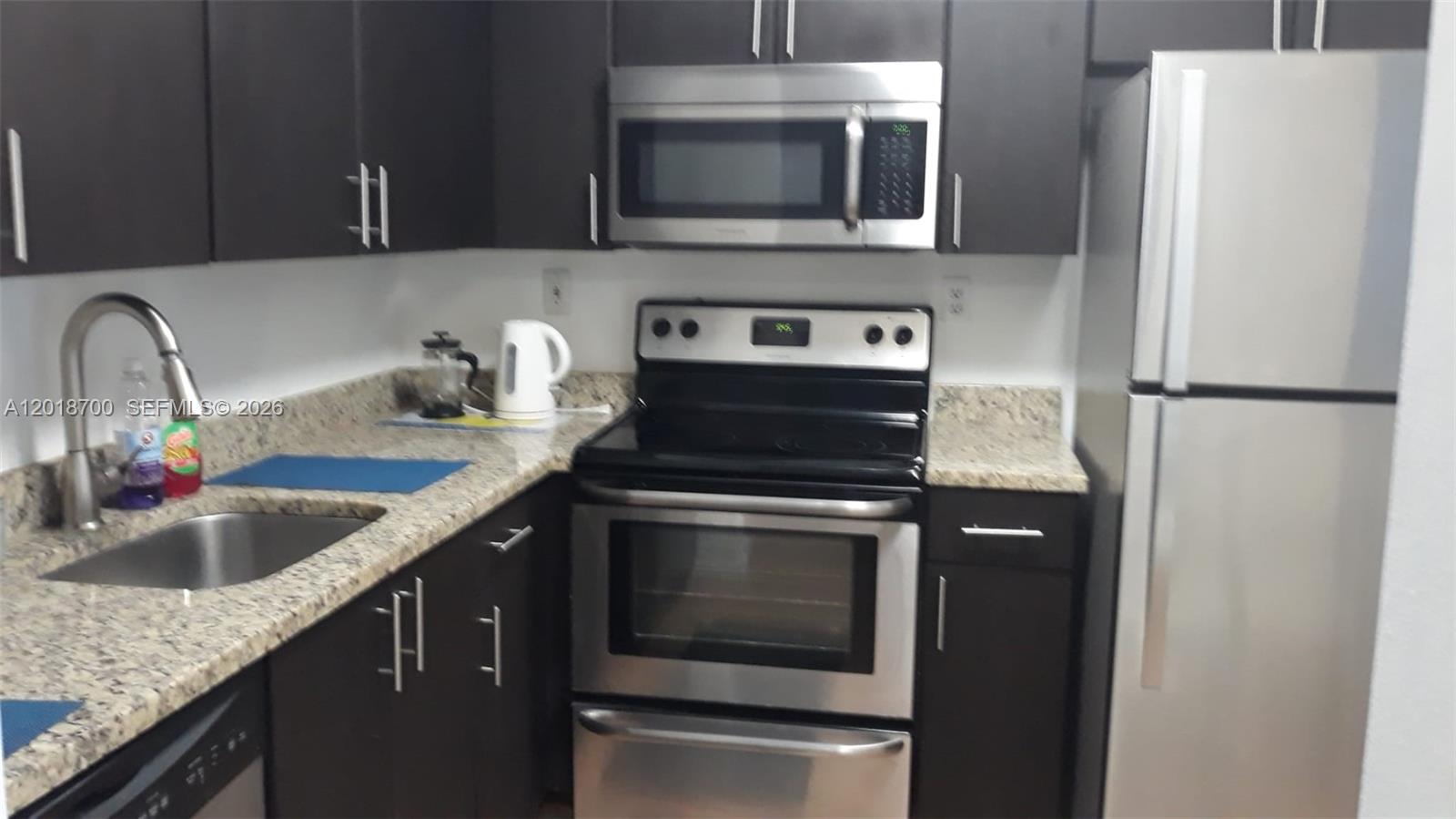 A kitchen features dark cabinets, stainless steel appliances, and speckled granite countertops — AVENTURA, FL