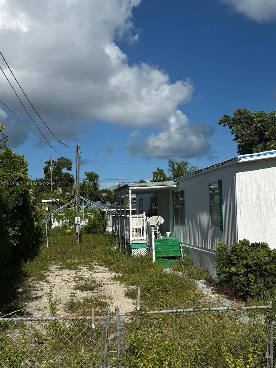 A white mobile home with a green porch and a gravel yard under a blue sky — 13 Judy Pl, Key Largo FL 33037, KEY LARGO, FL