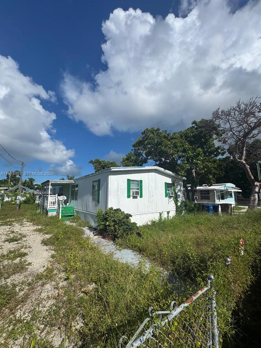 A white mobile home with green shutters sits on a grassy lot under a sky — 13 Judy Pl, Key Largo FL 33037, KEY LARGO, FL