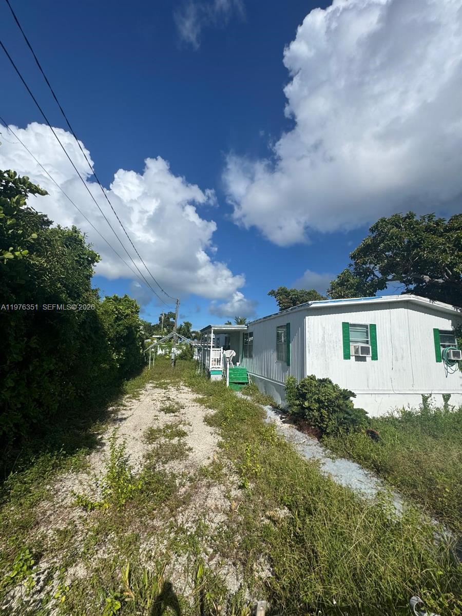 A white mobile home sits beside a gravel driveway under a bright blue sky — 13 Judy Pl, Key Largo FL 33037, KEY LARGO, FL