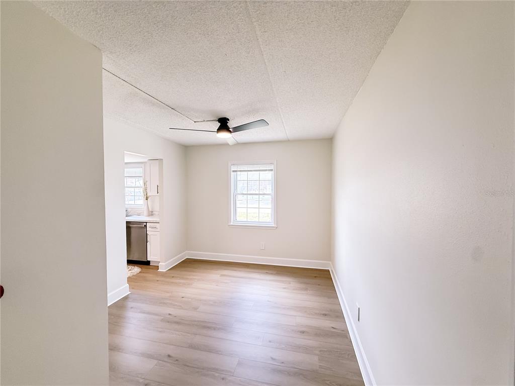 An empty room features light wood-look flooring, white walls, a ceiling fan, and a window — 1275 85TH AVENUE UNIT 1275B, ST PETERSBURG, FL