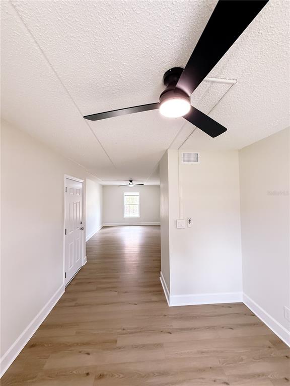 An interior view shows a room with light wood-look flooring, white walls, and ceiling fans — 1275 85TH AVENUE UNIT 1275B, ST PETERSBURG, FL