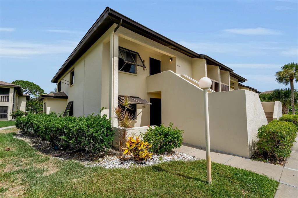 An exterior view of a two-story apartment building with beige stucco walls and stairs — 4644 LONGWATER UNIT 97, SARASOTA, FL