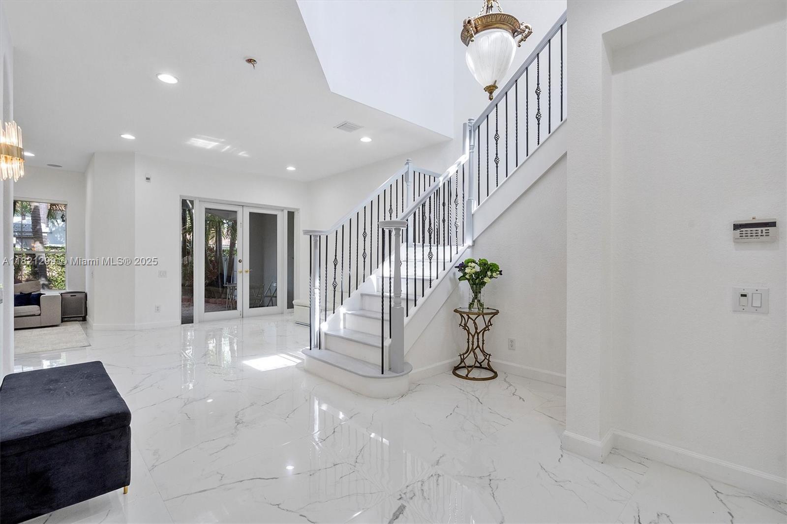A bright foyer features white marble floors, a staircase with black railings, and a chandelier — 1382 Harbor Vw W, Hollywood FL 33019, HOLLYWOOD, FL