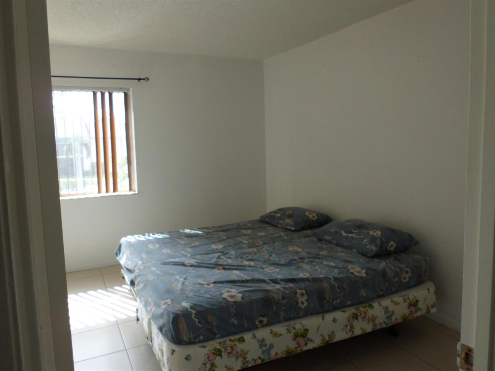 A bedroom with a floral-patterned bed, tile flooring, and a window with vertical blinds — 121 Lake Pine Circle # 2, FL 33463, FL