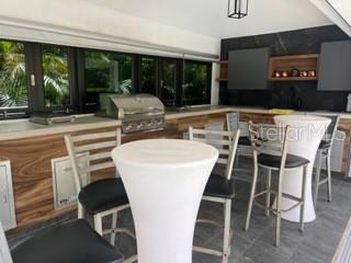 An outdoor kitchen features a built-in grill, wood-look cabinetry, and high-top tables with bar stools — Lot 8 PR-159 Km 1.9 Inter BO. UNIBON, MOROVIS, PR