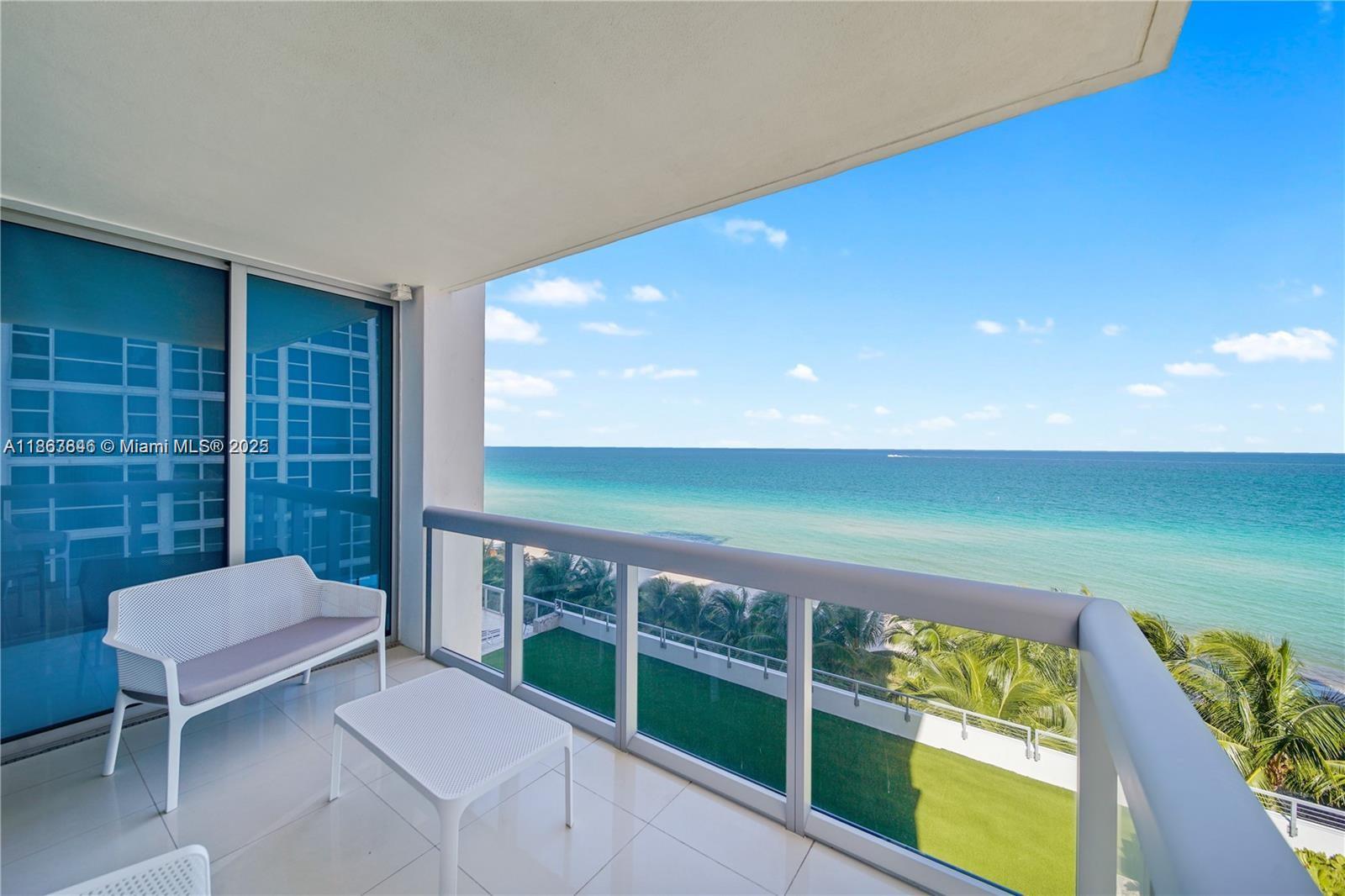 A balcony with white furniture overlooks the ocean and a lower green terrace — 6899 Collins Ave # 808, Miami Beach FL 33141, MIAMI BEACH, FL