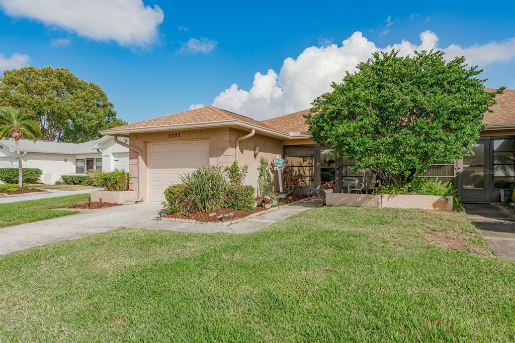 A single-story house with a tan stucco exterior, a one-car garage, and a front lawn — 3305 GORSE COURT, PALM HARBOR, FL