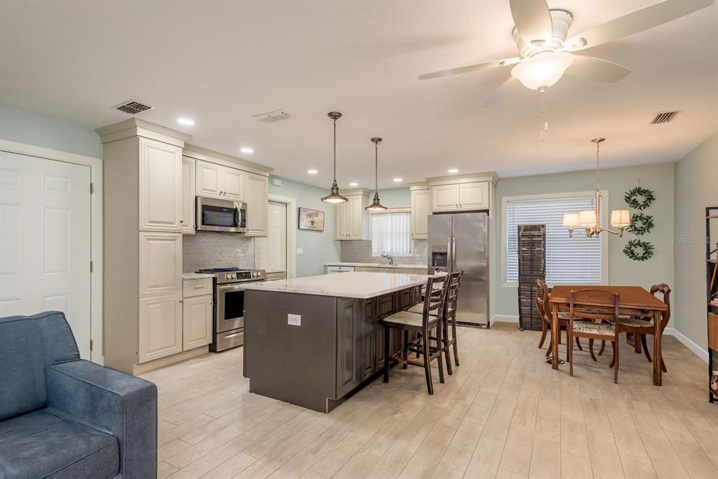 A kitchen features a dark gray island, light-colored cabinets, stainless steel appliances, and a dining area — 3305 GORSE COURT, PALM HARBOR, FL