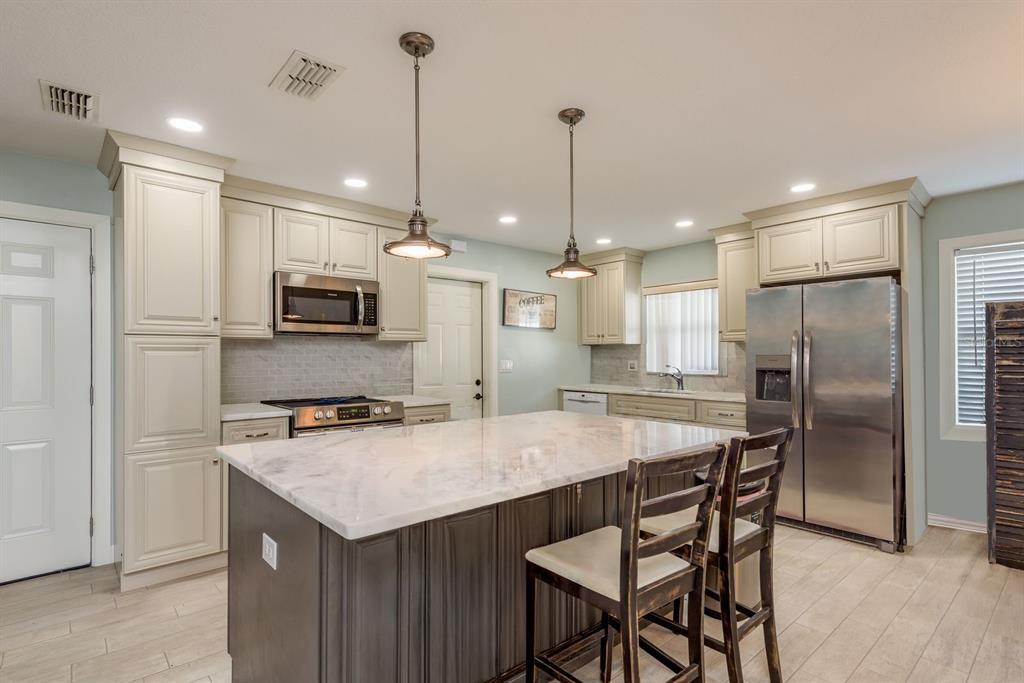 A kitchen features a dark wood island with marble countertops, stainless steel appliances, and cream cabinets — 3305 GORSE COURT, PALM HARBOR, FL