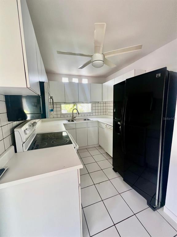 A kitchen features white cabinets, a black refrigerator, a stove, and white tiled flooring — YAMIL GALIB PASEO LOS ROBLES UNIT 1614, MAYAGUEZ, PR