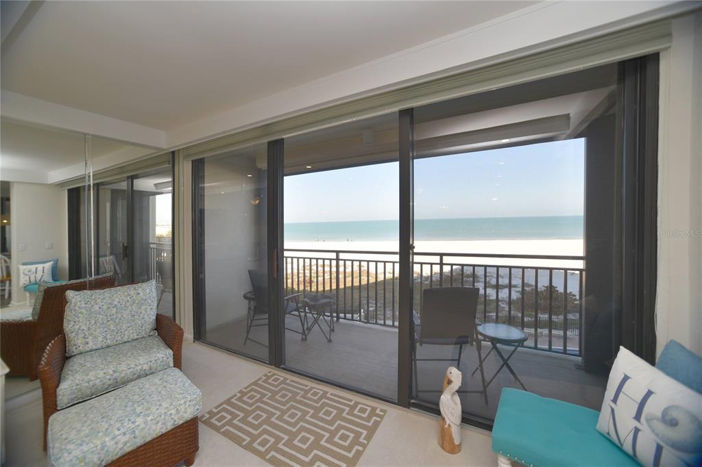 A sunroom features a wicker chair, a geometric rug, and sliding doors overlooking the beach — 3820 GULF BOULEVARD UNIT 306, ST PETE BEACH, FL