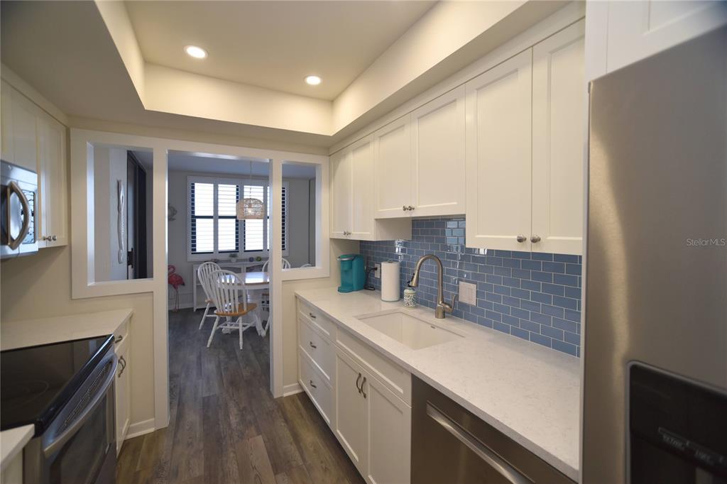 A kitchen with white cabinets, blue subway tile backsplash, and a view into a dining area — 3820 GULF BOULEVARD UNIT 306, ST PETE BEACH, FL
