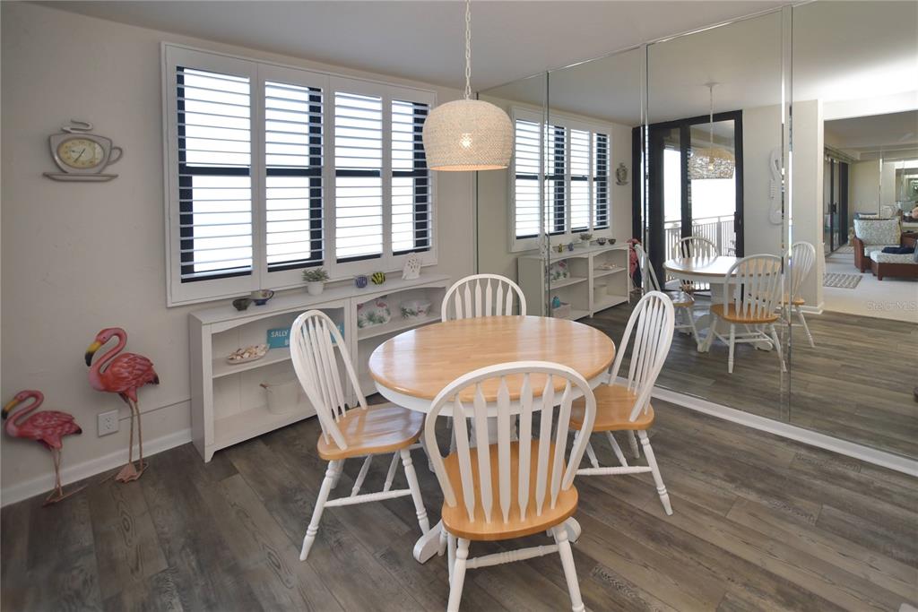 A dining area features a round wooden table, white spindle chairs, and mirrored wall panels — 3820 GULF BOULEVARD UNIT 306, ST PETE BEACH, FL