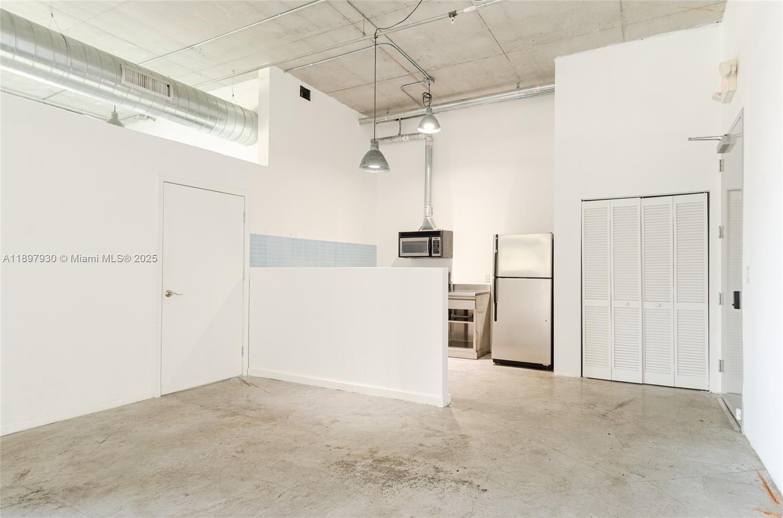 An industrial-style studio apartment features a concrete ceiling, exposed ductwork, and a small kitchenette — 250 NW 23 # 202, Miami FL 33127, MIAMI, FL