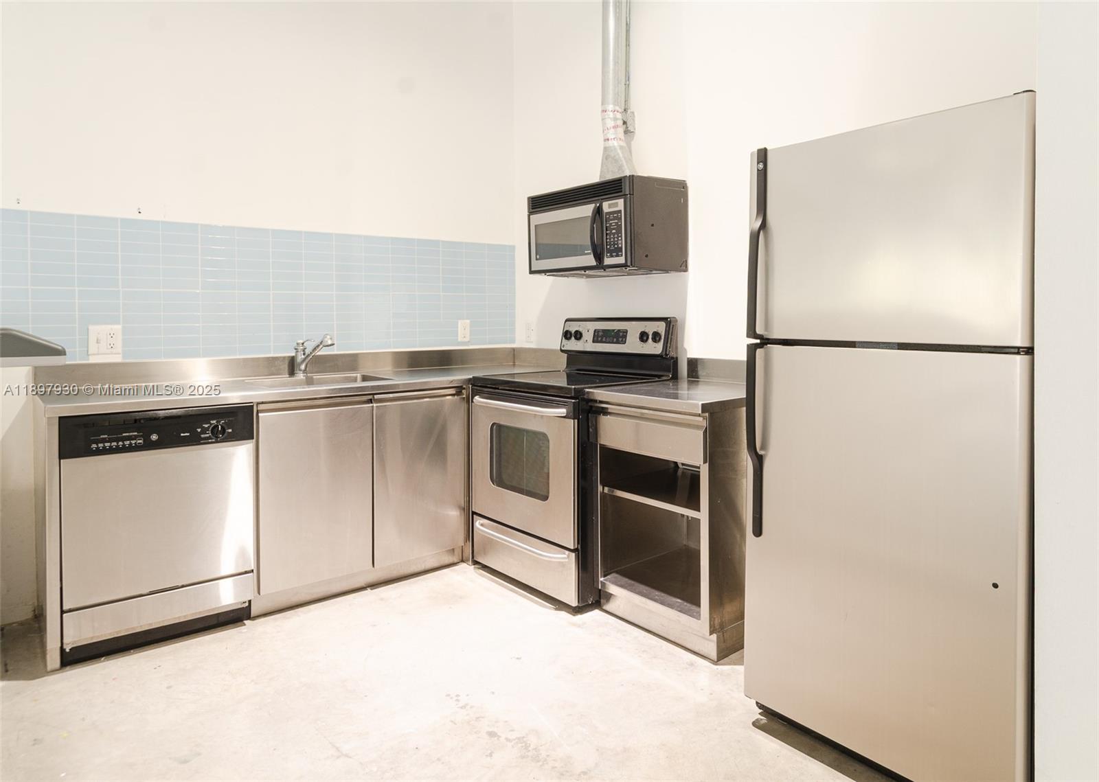 A kitchen features stainless steel appliances, metal cabinetry, and a light blue tiled backsplash — 250 NW 23 # 202, Miami FL 33127, MIAMI, FL
