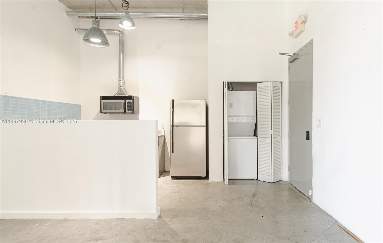 A kitchen area features a stainless steel refrigerator, a stacked washer-dryer, and concrete flooring — 250 NW 23 # 202, Miami FL 33127, MIAMI, FL