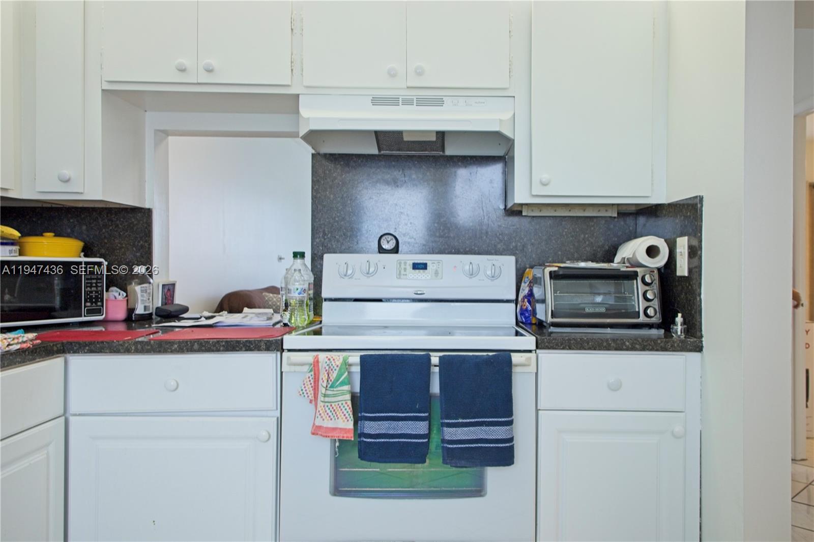 A white kitchen features a stove, range hood, and dark countertops with white cabinetry — 2309 Park Ln # 304, Hollywood FL 33021, HOLLYWOOD, FL