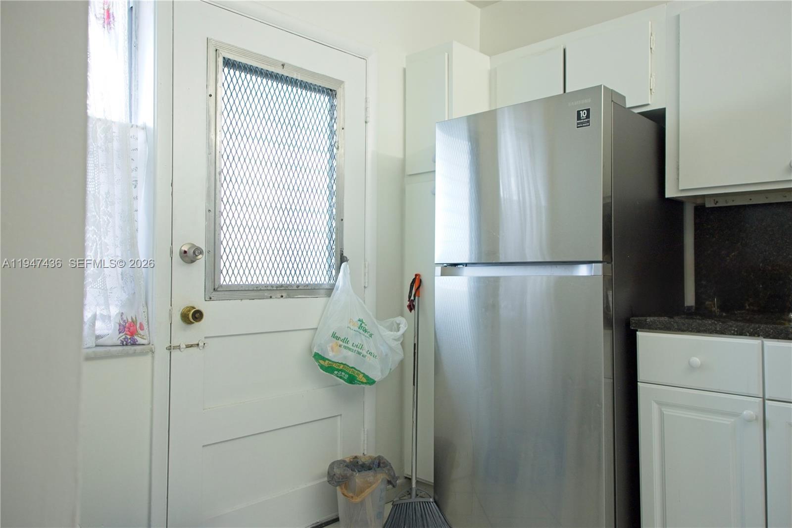 A kitchen features a stainless steel refrigerator, white cabinets, and a door with a screen — 2309 Park Ln # 304, Hollywood FL 33021, HOLLYWOOD, FL