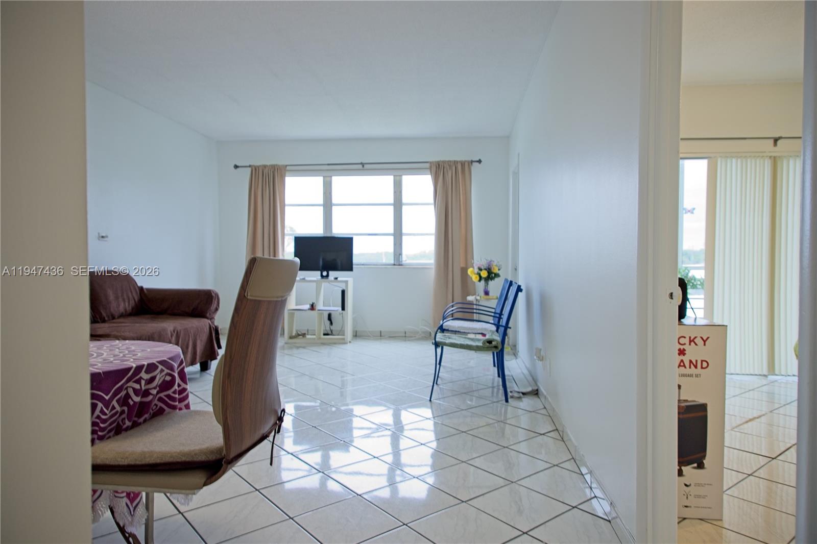A living room features white tiled floors, a brown sofa, and a window with curtains — 2309 Park Ln # 304, Hollywood FL 33021, HOLLYWOOD, FL