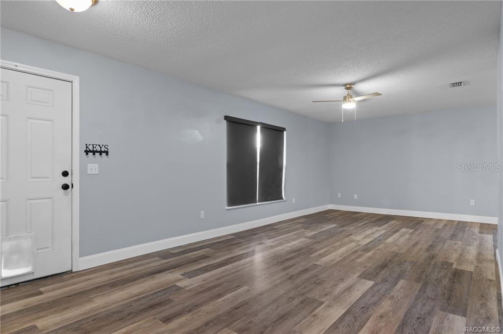 An empty room with light blue walls, wood-look flooring, a ceiling fan, and a door — 1317 CARL STREET, INVERNESS, FL