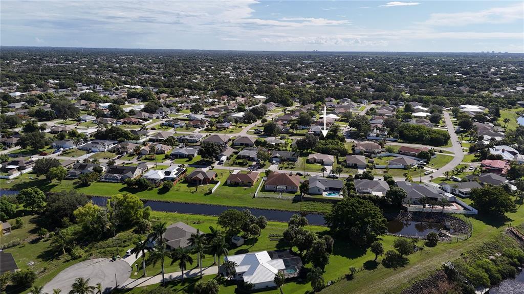 An aerial view shows a suburban neighborhood with houses, a canal, and green spaces — 2668 SW CAMEO BOULEVARD, PORT ST LUCIE, FL