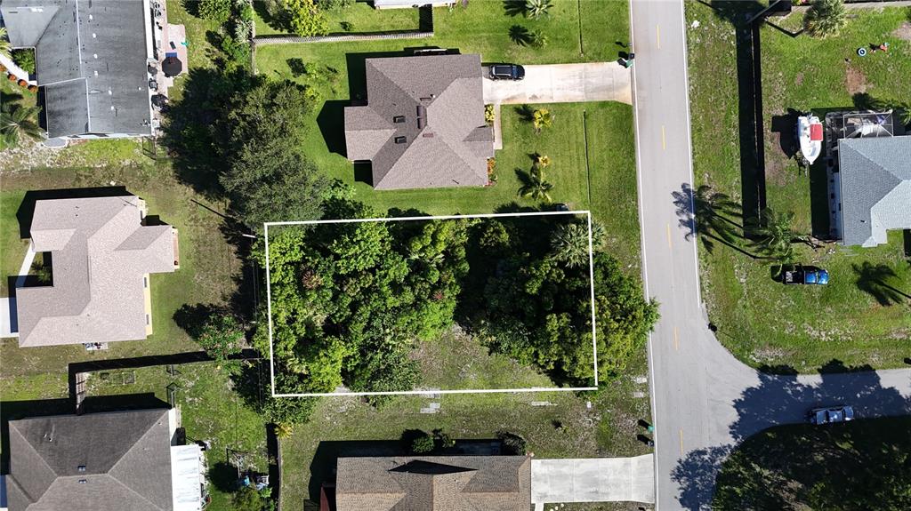 An aerial view shows a rectangular, tree-covered vacant lot situated between two residential houses — 2668 SW CAMEO BOULEVARD, PORT ST LUCIE, FL