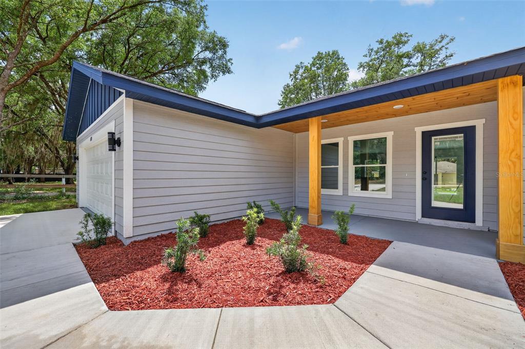A gray house exterior features a blue door, wood support posts, and a red mulch garden — 13761 SW 114TH PLACE, DUNNELLON, FL