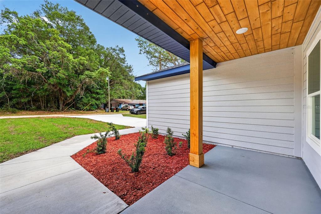 A covered concrete porch with a wood-paneled ceiling and a small red-mulched garden bed — 13761 SW 114TH PLACE, DUNNELLON, FL