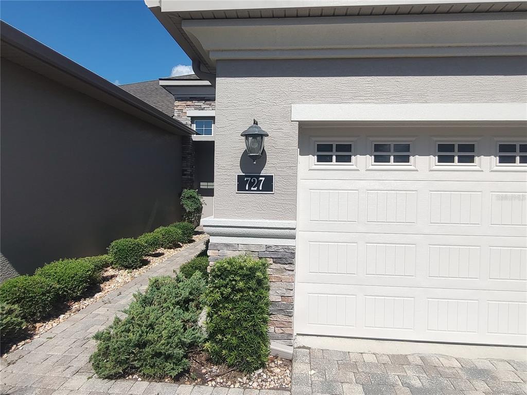 A beige house exterior features a white garage door, stone accents, and a paved walkway — 727 ALDENHAM LANE, ORMOND BEACH, FL