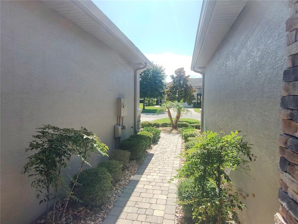 A paved walkway leads between two stucco house walls toward a street and landscaping — 727 ALDENHAM LANE, ORMOND BEACH, FL