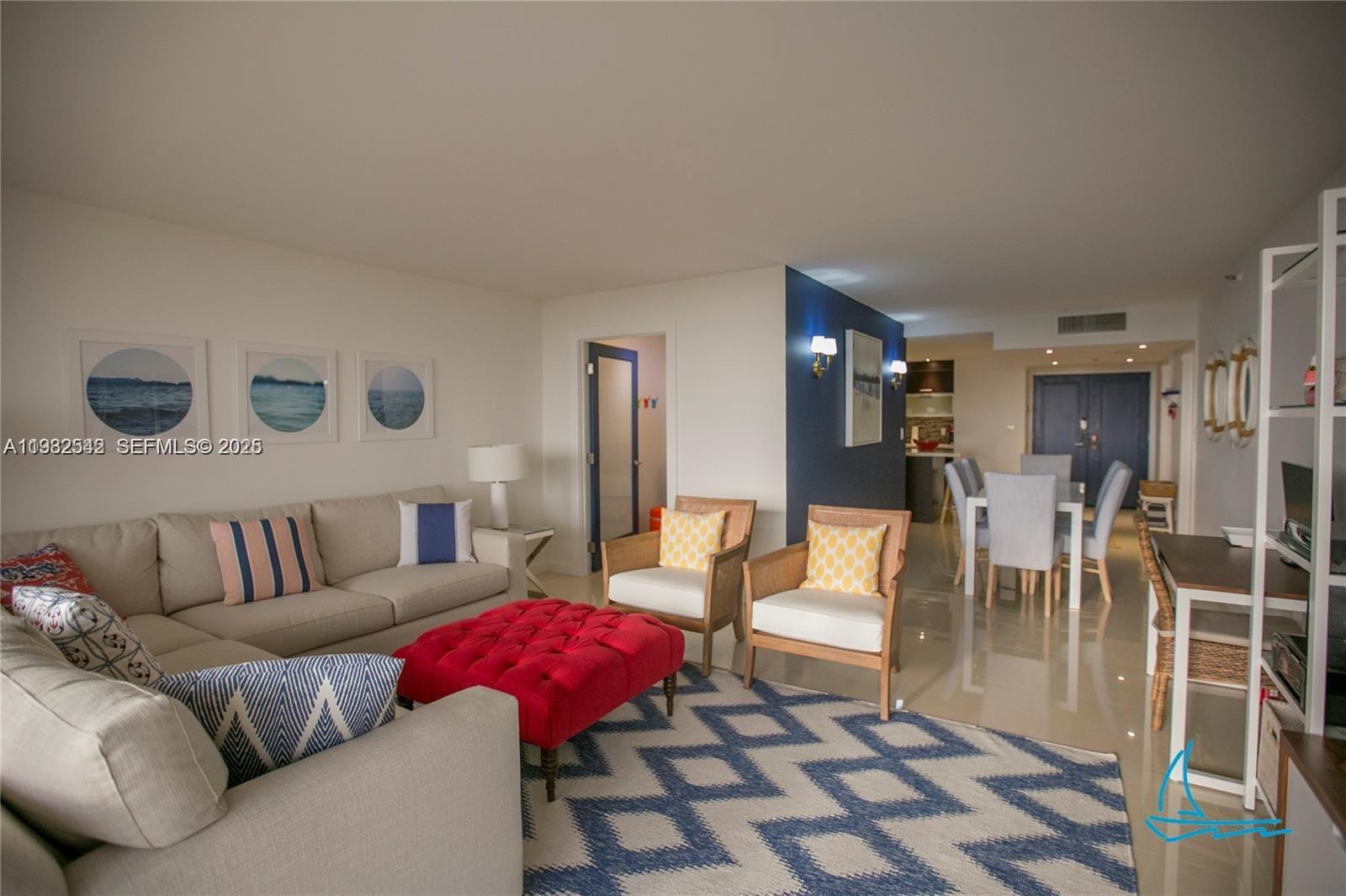 A living room features a beige sectional sofa, a red ottoman, and two wooden armchairs — 8877 Collins Ave # 805, Surfside FL 33154, SURFSIDE, FL