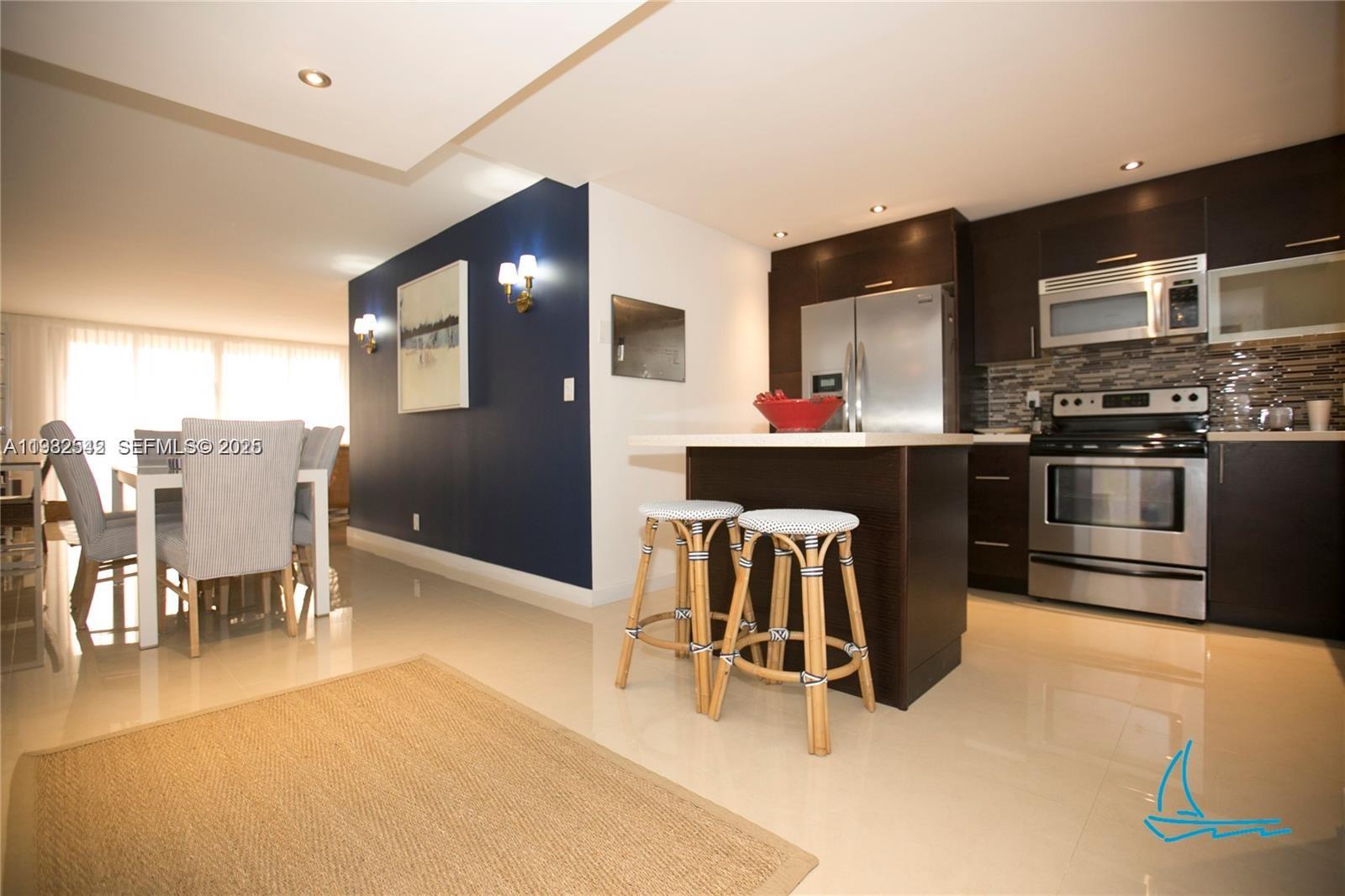 A kitchen with dark wood cabinets and a central island sits beside a dining area — 8877 Collins Ave # 805, Surfside FL 33154, SURFSIDE, FL