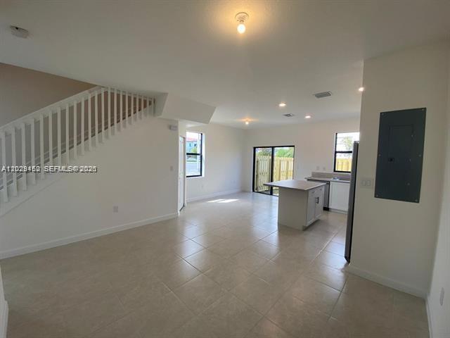 An open-concept living area features a staircase, tile flooring, and a kitchen with an island — 593 NE 208th Ter, Miami FL 33179, MIAMI, FL