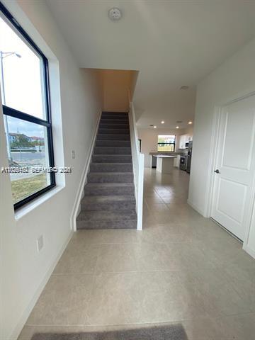 A view of a carpeted staircase leading upward, with a tiled entryway and kitchen beyond — 593 NE 208th Ter, Miami FL 33179, MIAMI, FL