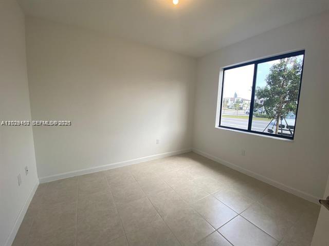 An empty room with light-colored tile flooring, white walls, and a large window — 593 NE 208th Ter, Miami FL 33179, MIAMI, FL