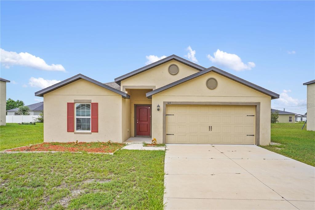 A single-story house with a tan stucco exterior, red front door, and a two-car garage — 123 VIOLET COURT, POINCIANA, FL
