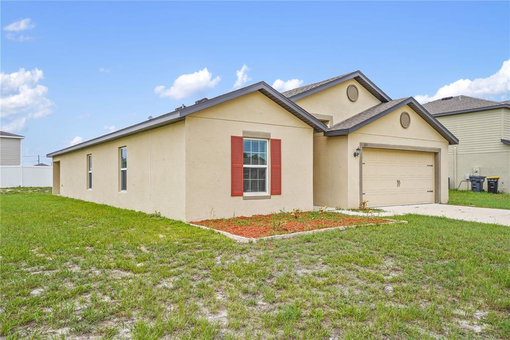 A single-story house with tan stucco siding, a two-car garage, and red window shutters — 123 VIOLET COURT, POINCIANA, FL