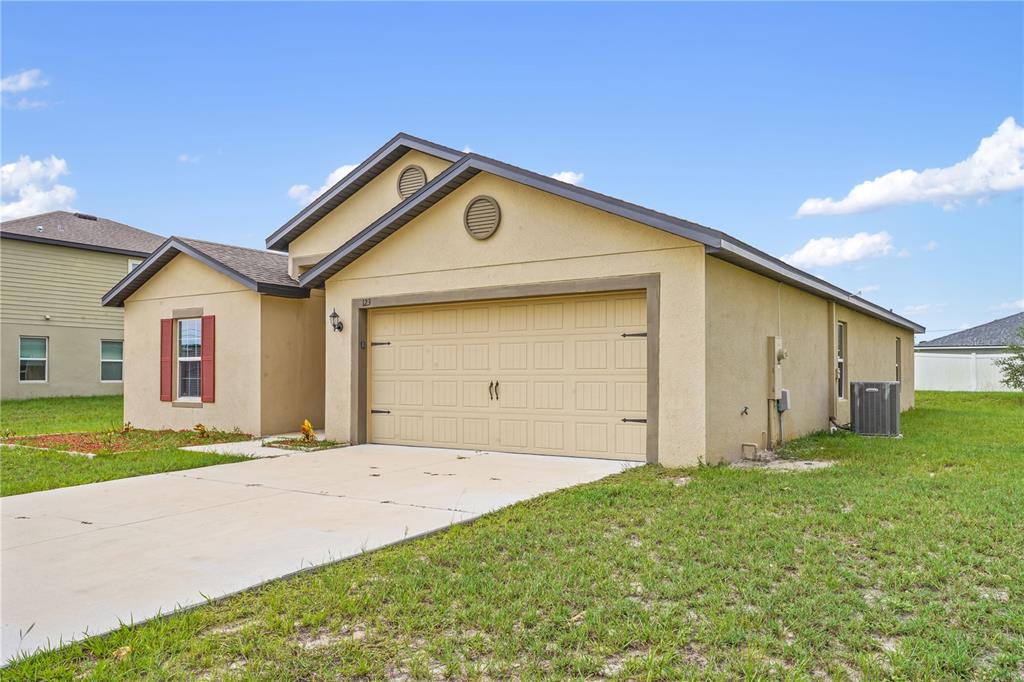 A single-story house with a tan stucco exterior, a two-car garage, and a concrete driveway — 123 VIOLET COURT, POINCIANA, FL