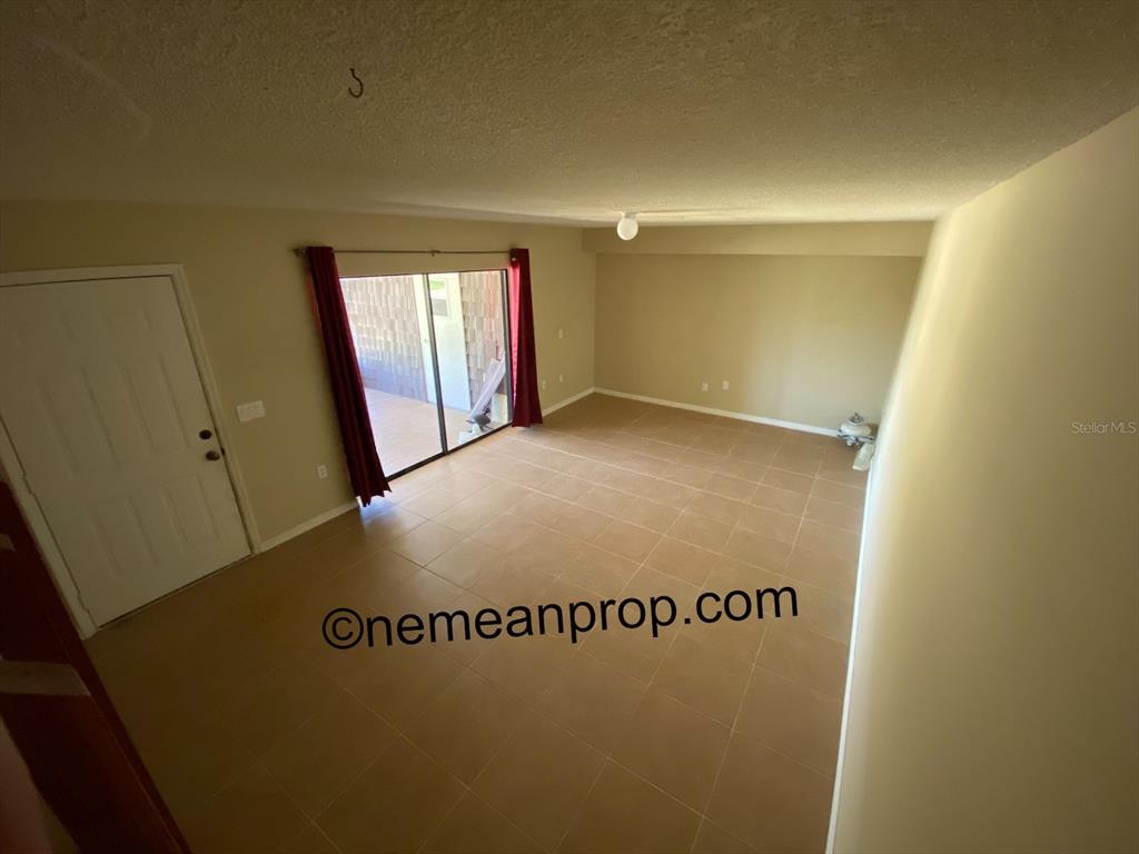 An empty room features tan tile flooring, beige walls, and a sliding glass door — 2949 POPLAR AVENUE, LEESBURG, FL
