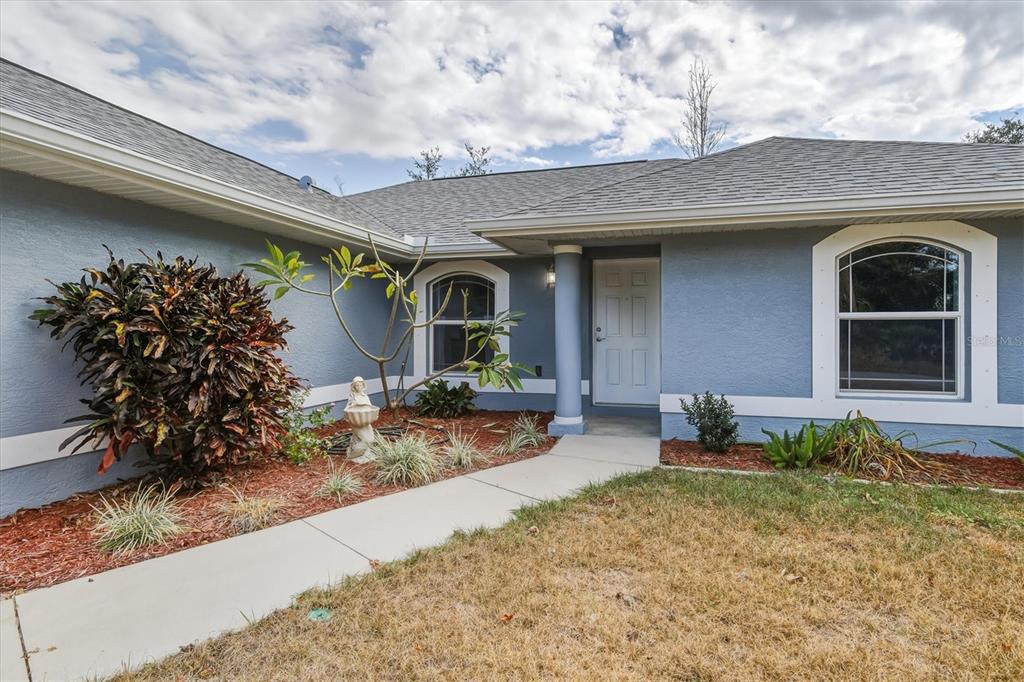 The exterior of a blue house features a front door, arched windows, and landscaping — 3447 NADASKY AVENUE, NORTH PORT, FL