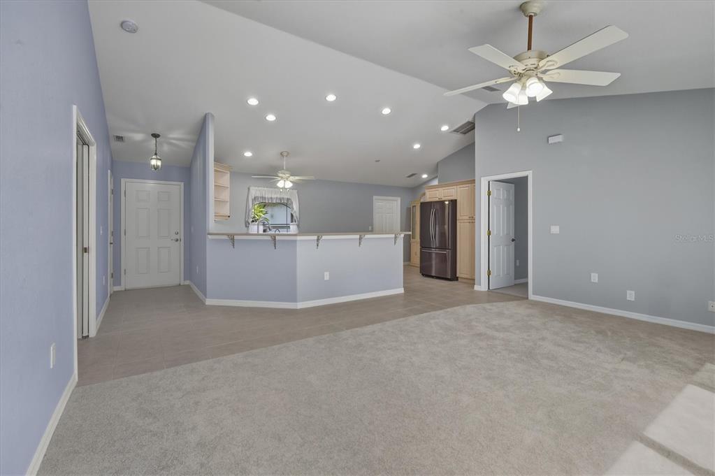 A spacious living room with carpeted flooring opens to a kitchen with a breakfast bar — 3447 NADASKY AVENUE, NORTH PORT, FL