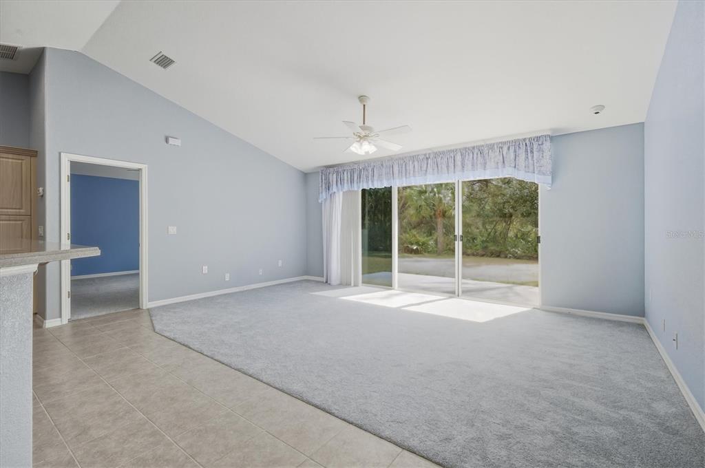 A living room with light blue walls, gray carpeting, a ceiling fan, and sliding glass doors — 3447 NADASKY AVENUE, NORTH PORT, FL