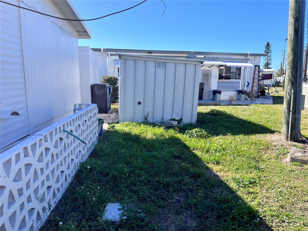 A metal storage shed sits in a grassy backyard next to a white lattice wall — 207 51ST AVENUE PLAZA W UNIT 3, BRADENTON, FL