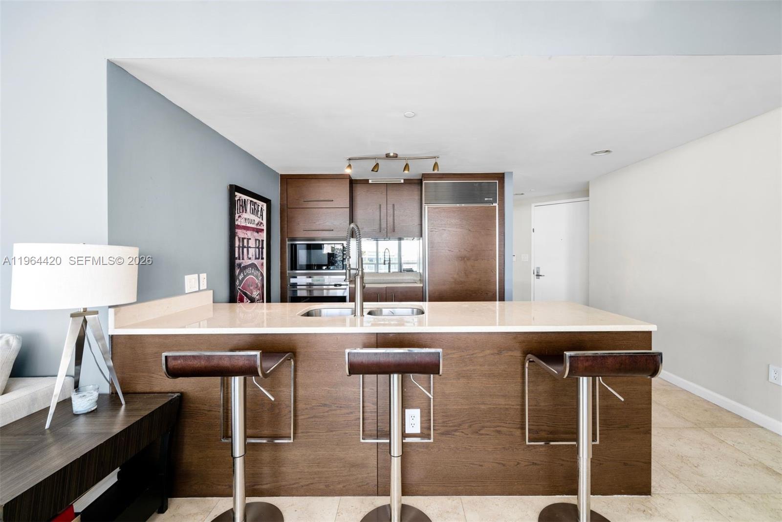 A kitchen features a large island with three bar stools and dark wood cabinetry — 465 Brickell Ave # 5302, Miami FL 33131, MIAMI, FL