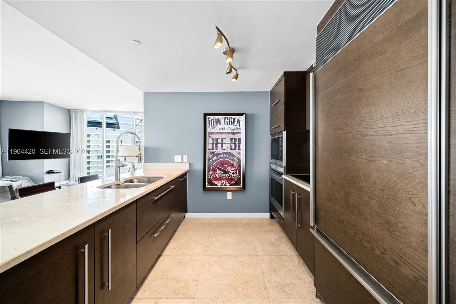 A modern galley kitchen features dark wood cabinetry, light countertops, and a framed wall poster — 465 Brickell Ave # 5302, Miami FL 33131, MIAMI, FL