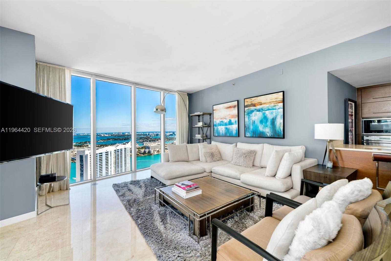 A living room features a white sectional sofa, a coffee table, and floor-to-ceiling windows — 465 Brickell Ave # 5302, Miami FL 33131, MIAMI, FL