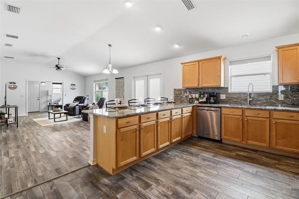 A kitchen with wood cabinets and granite countertops opens into a living room with flooring — 2264 WAYLAND STREET, THE VILLAGES, FL