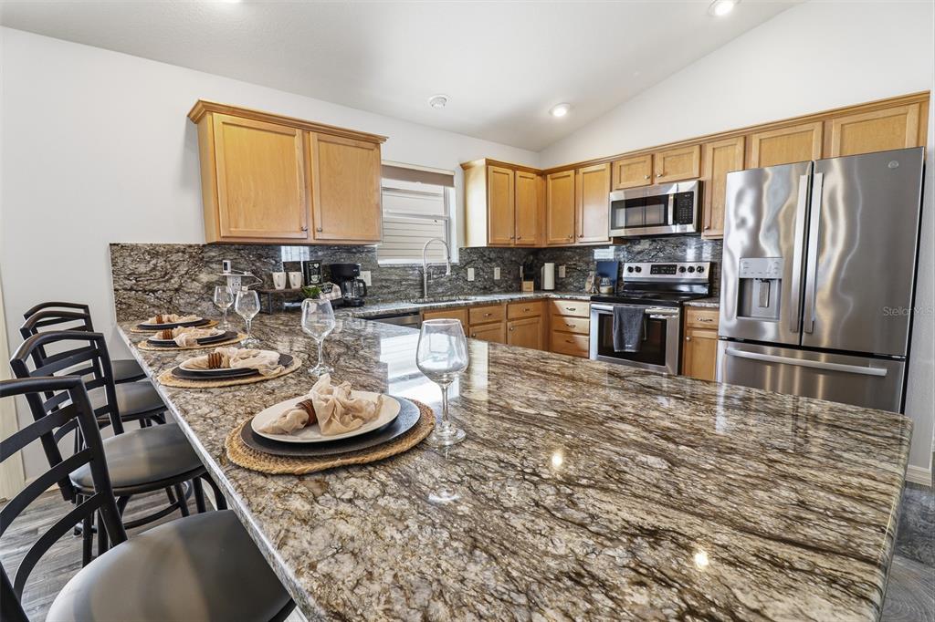 A kitchen features light wood cabinets, granite countertops, stainless steel appliances, and a breakfast bar — 2264 WAYLAND STREET, THE VILLAGES, FL