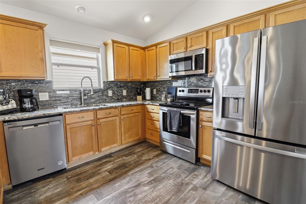 A kitchen features wood cabinets, granite countertops, stainless steel appliances, and wood-look flooring — 2264 WAYLAND STREET, THE VILLAGES, FL